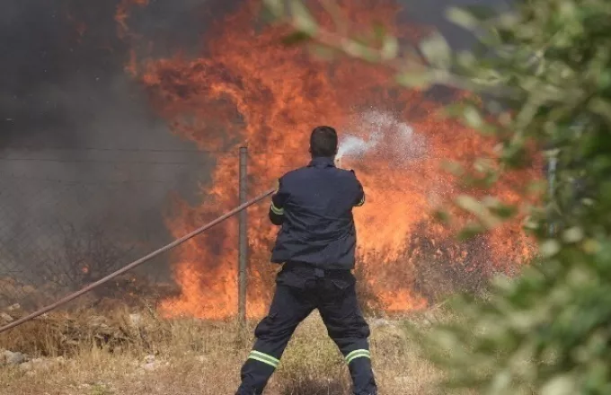 Πυροσβέστης με μάνικα προσπαθεί να σβήσει τη φωτιά 