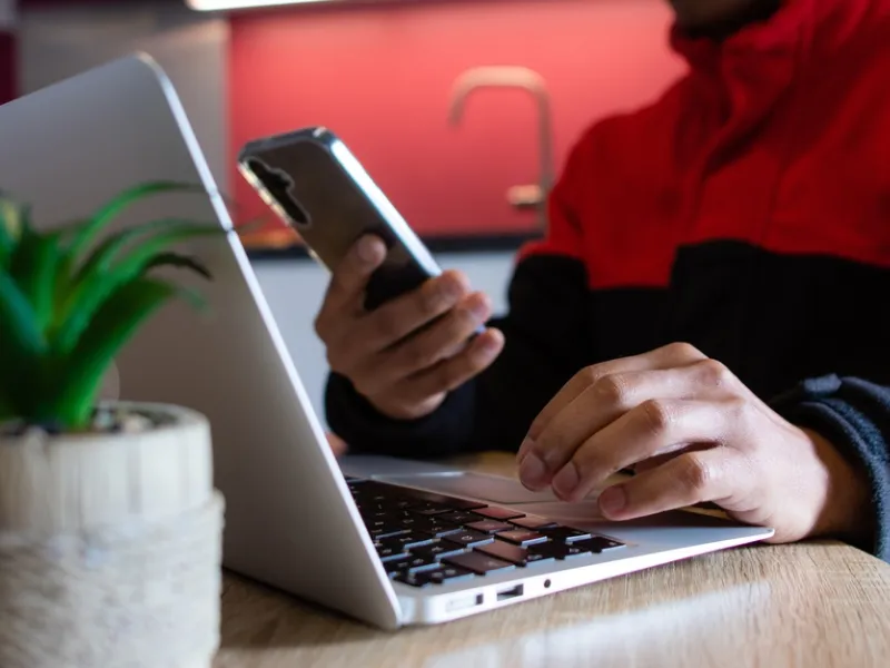 Man typing on a laptop and holding a smartphone